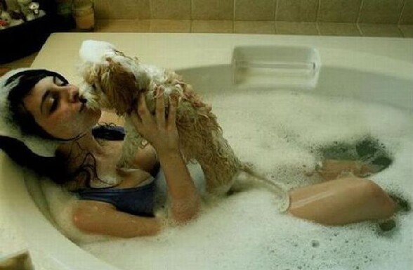 Un fille habillee dans la baignoire prend son bain avec son chien