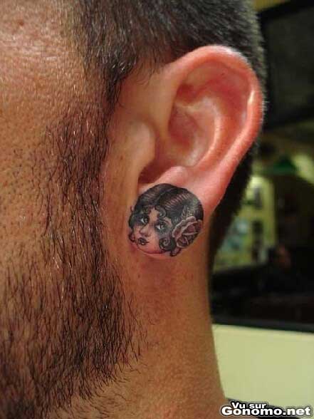 Un petit visage de femme tatoue sur le lobe de cette oreille